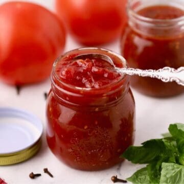 Two jars full off tomato jam, one with a small spoon in it.