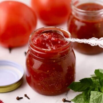 Two jars full off tomato jam, one with a small spoon in it.