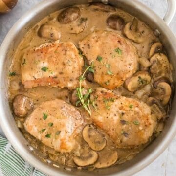 A metal skillet with pan seared pork chops resting in a mushroom pan sauce.