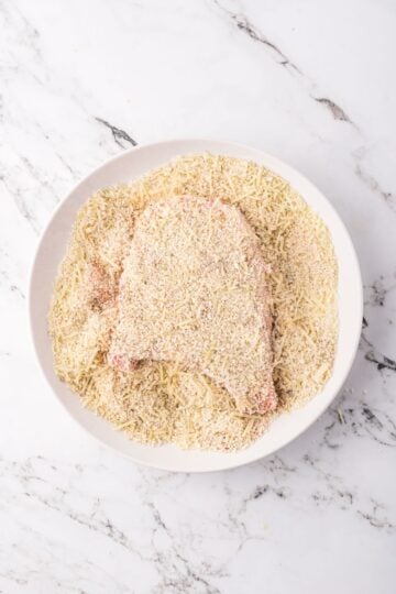 A pork chop in a bowl with panko, parmesan, and seasonings.