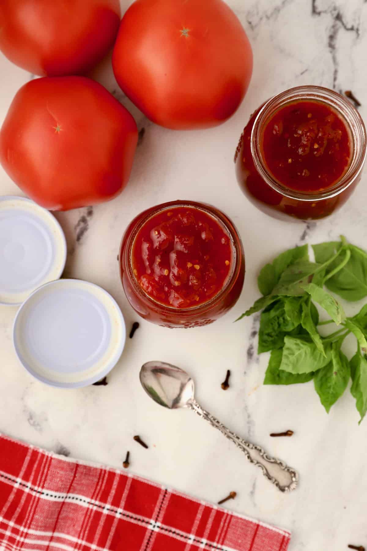 Jars of tomato jam with lids and fresh tomatoes in the back.