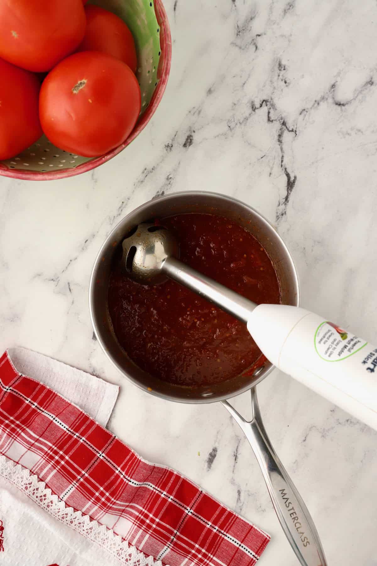Cooked tomato jam in a saucepan with an immersion blender, pureeing the jam.