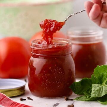 A jar of tomato jam with a spoon holding a serving of it.