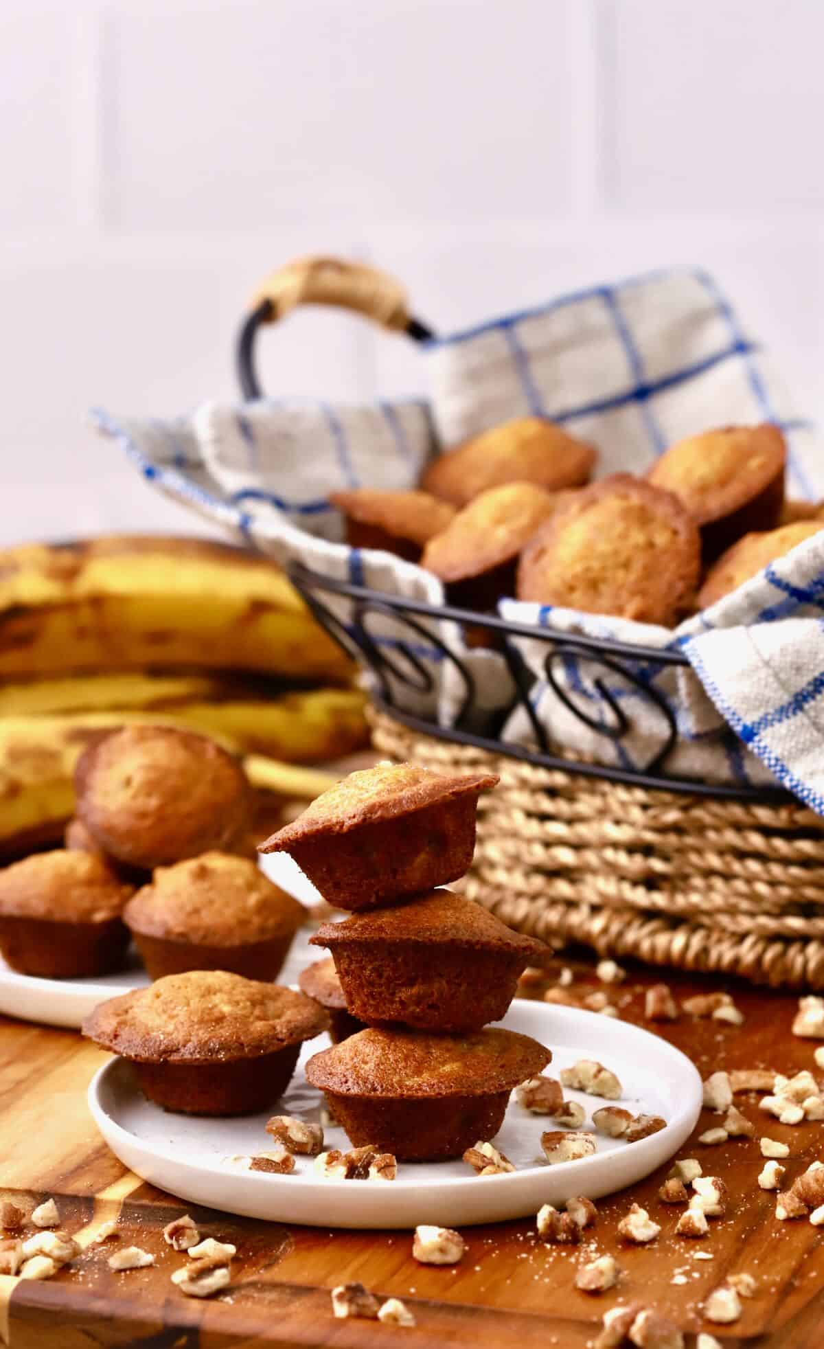 A stack of three banana nut mini muffins on a plate with the basket of muffins behind it.