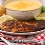 A blackened redfish fillet on a plate with a bowl of cheese grits.