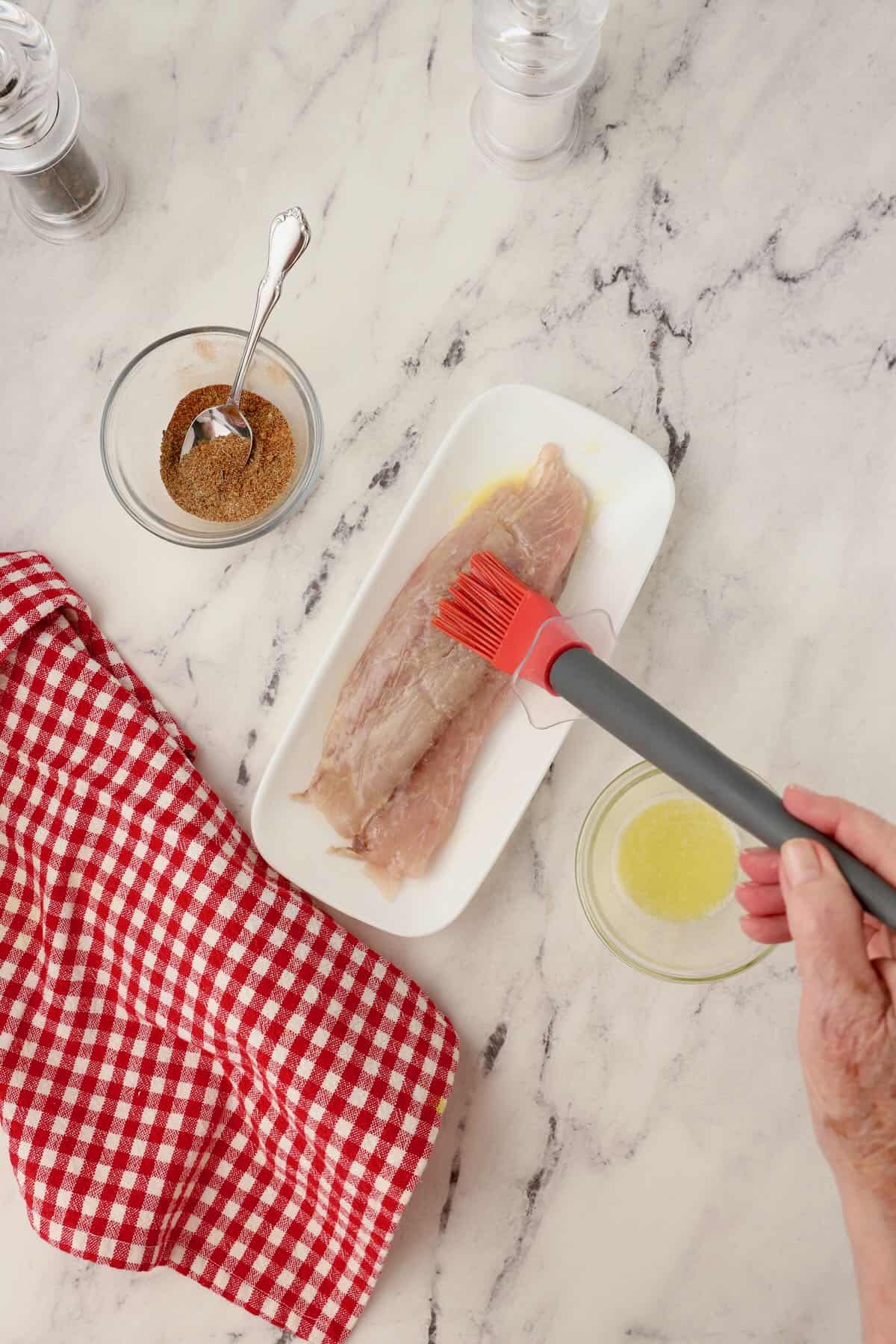Coating a redfish fillet with melted butter with a pastry brush.