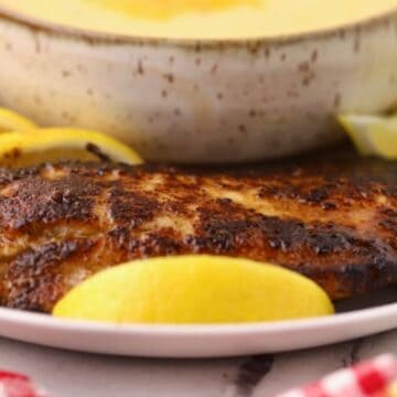 A blackened redfish fillet on a plate with a bowl of cheese grits.
