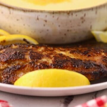 A blackened redfish fillet on a plate with a bowl of cheese grits.