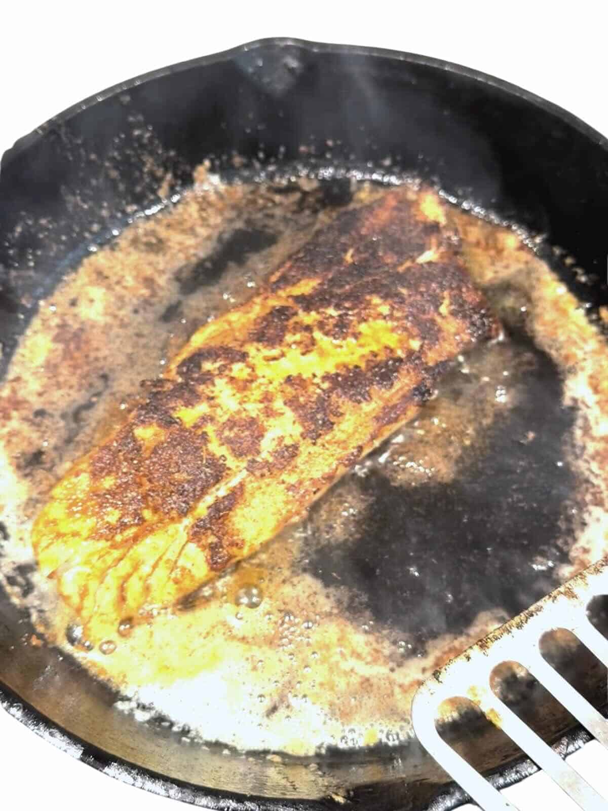 Blackened redfish fillet cooking in a cast iron skillet with a blackened crust.