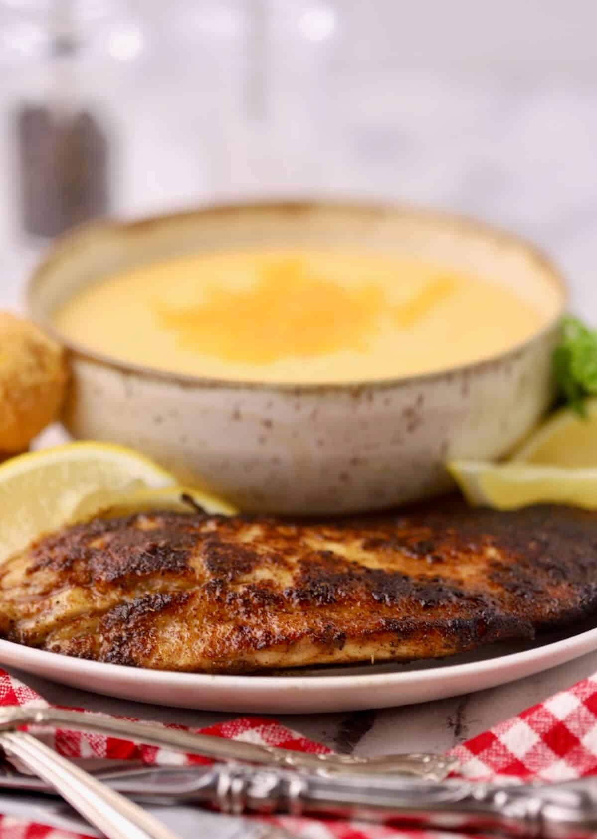 Blackened redfish on a plate with cheese grits and lemons.