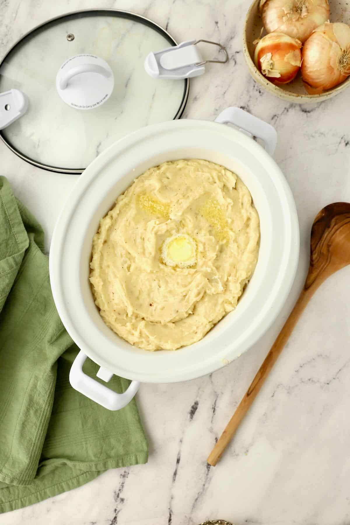 A crock pot full of creamy mashed potatoes with a melted pat of butter.