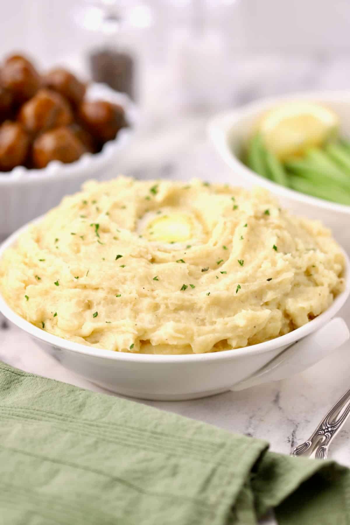 A large bowl of fluffy mashed potatoes topped with a pat of melted butter and garnished with chopped parsley.