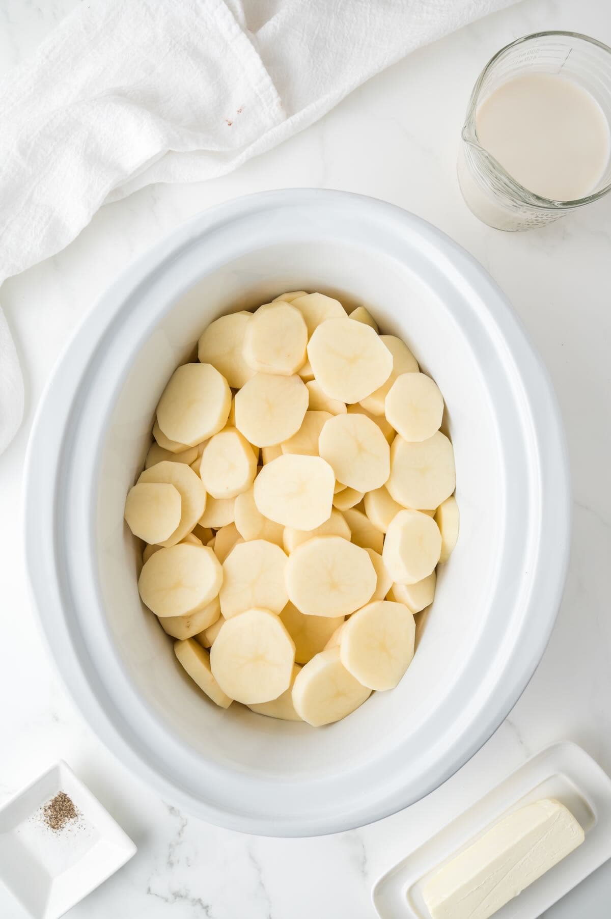 A white crock pot bowl full of sliced potatoes.