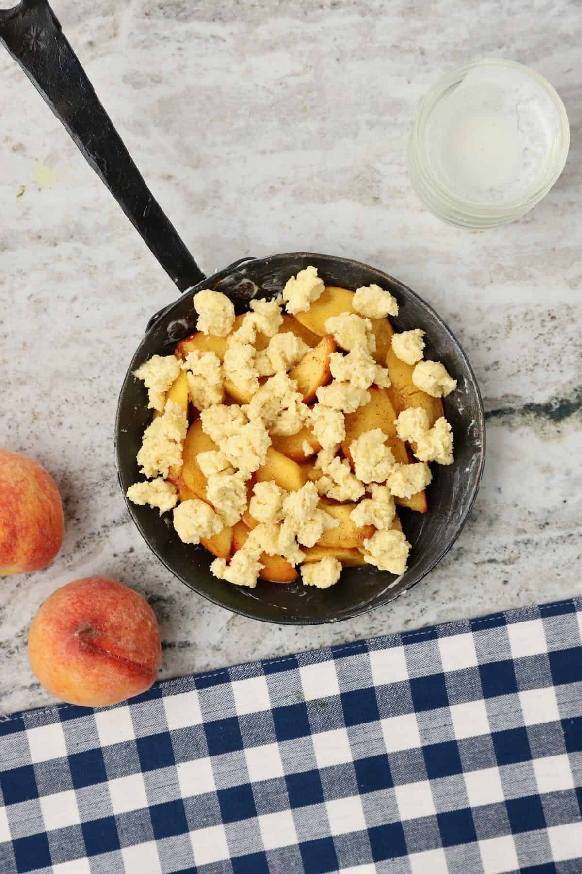 Cobbler assembled in a cast iron skillet with peaches and dough on the top.