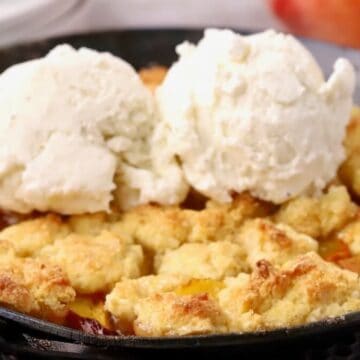 Small batch peach cornmeal cobbler for two topped with two scoops of vanilla ice cream in a cast-iron skillet