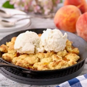 Small batch peach cornmeal cobbler for two topped with vanilla ice cream in a cast-iron skillet.