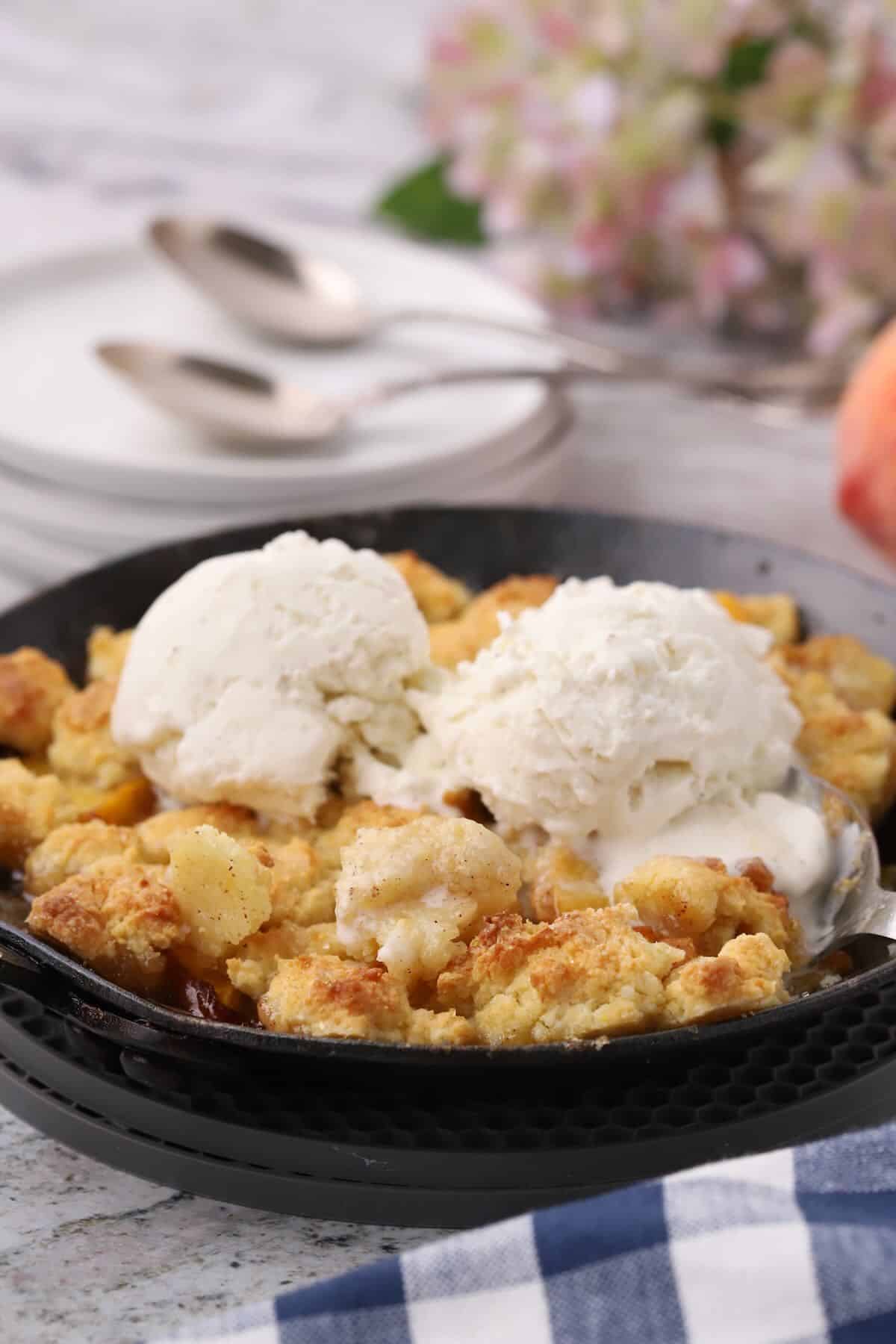 Small batch peach cornmeal cobbler for two topped with vanilla ice cream in a cast-iron skillet.