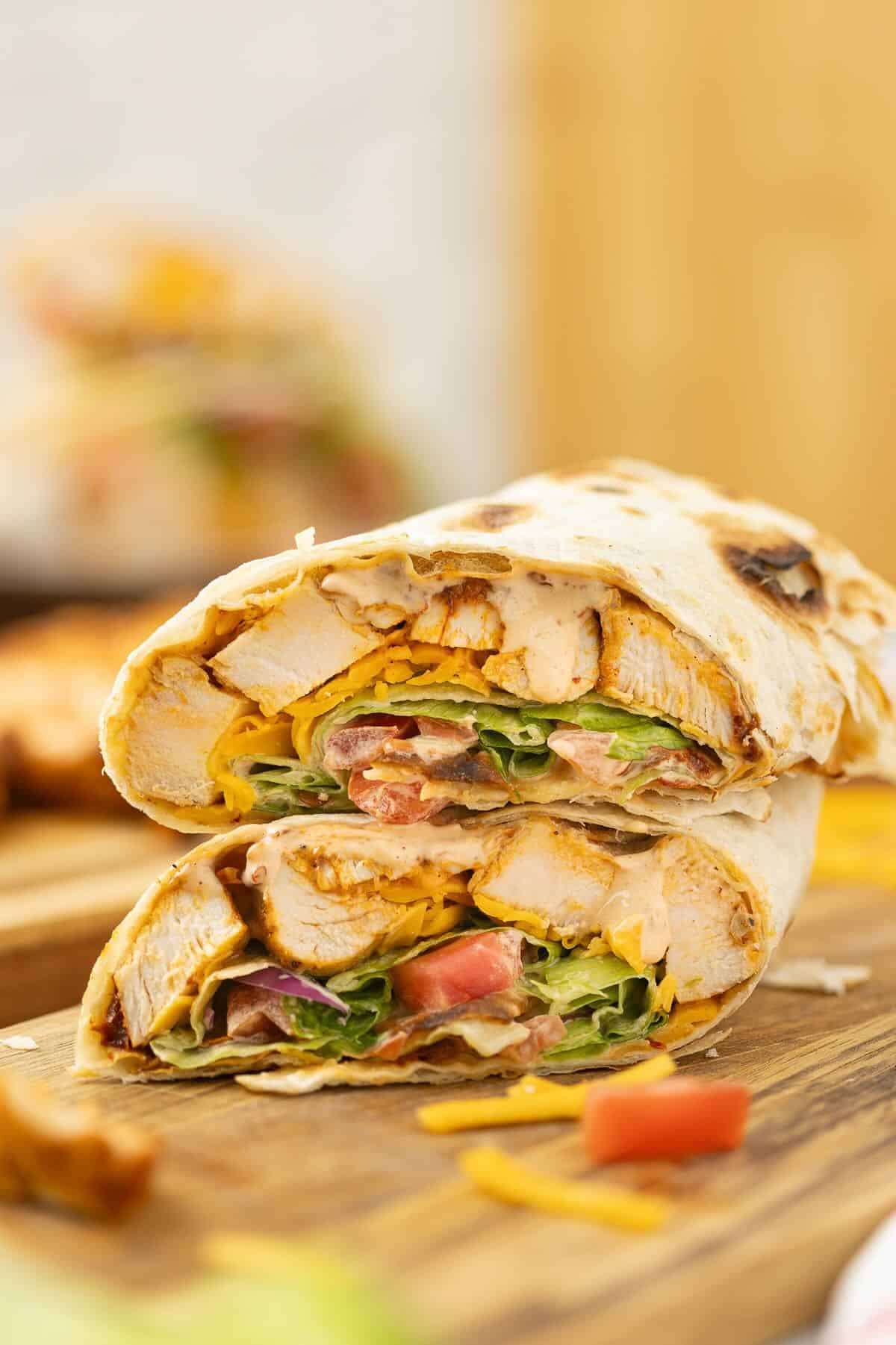 A grilled chicken wrap, cut in half, full of grilled chicken, lettuce, tomato, and shredded cheese, cut in half on a plate.