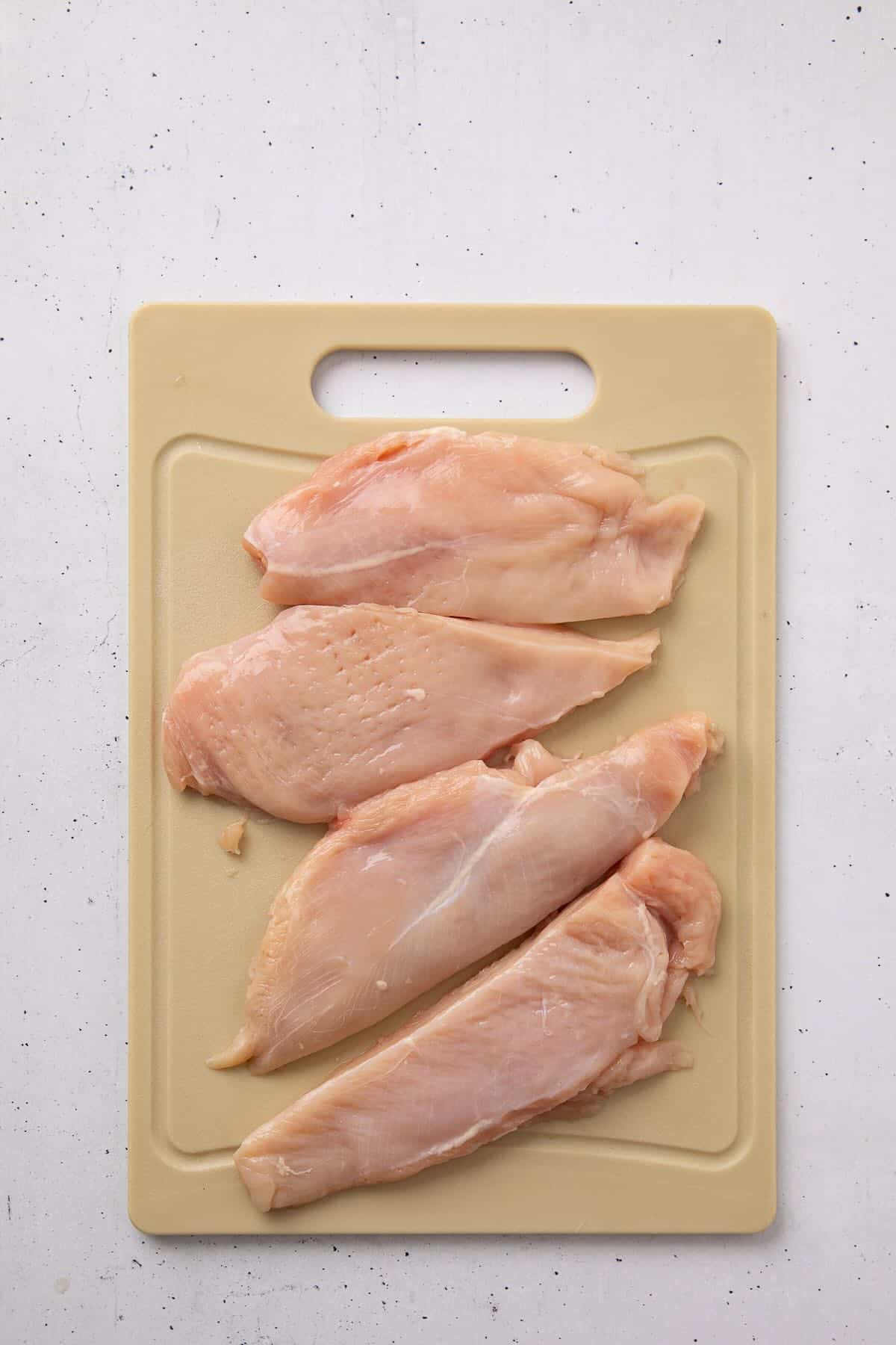 Two raw chicken breasts on a cutting board that have been pounded to an even thickness and cut in half to make four.