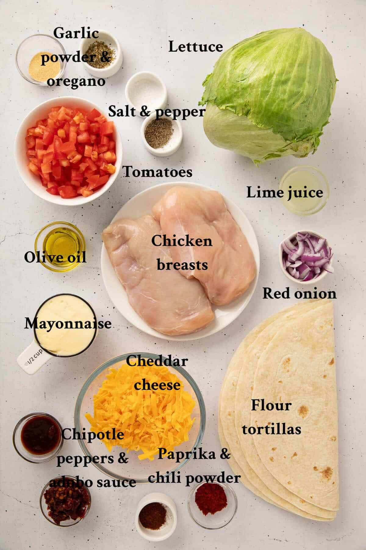 Ingredients to make grilled chicken wraps include, chicken breasts, tortillas, seasonings, lettuce, tomato, and chipotles with adobo sauce.
