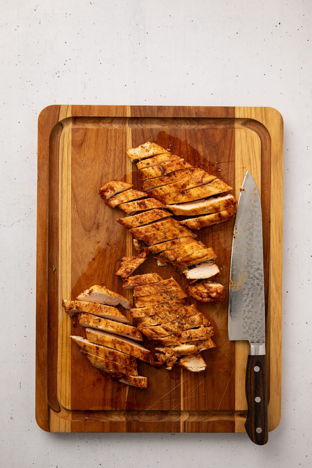 Grilled chicken breasts sliced against the grain on a cutting board.
