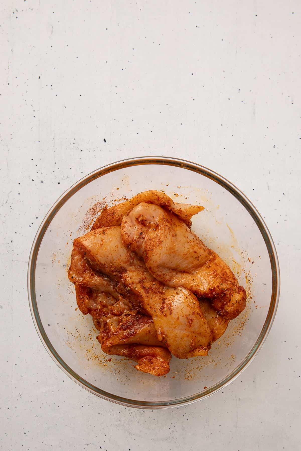 Ray chicken breasts coated with oil and seasonings in a bowl.