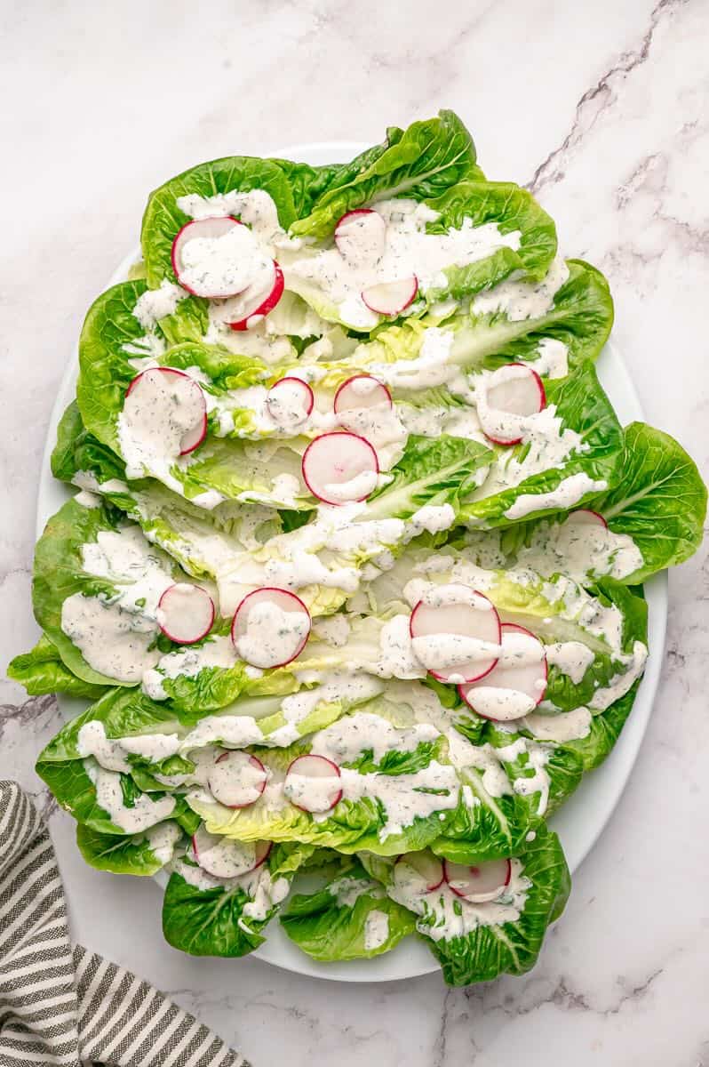 Little Gem Salad on a platter topped with sliced radishes and dressing.