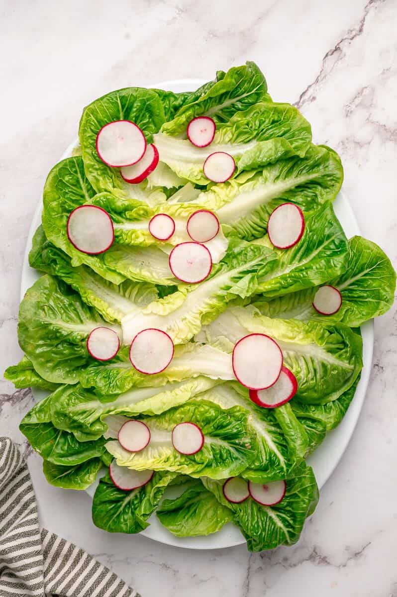 Little Gem lettuce leaves on a platter topped with sliced radishes.