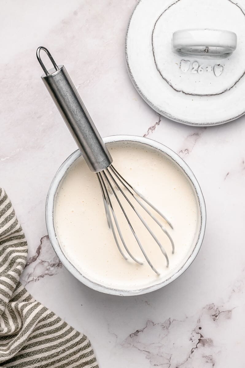 Coconut milk, mayonnaise, and apple cider vinegar in a bowl with a whisk.