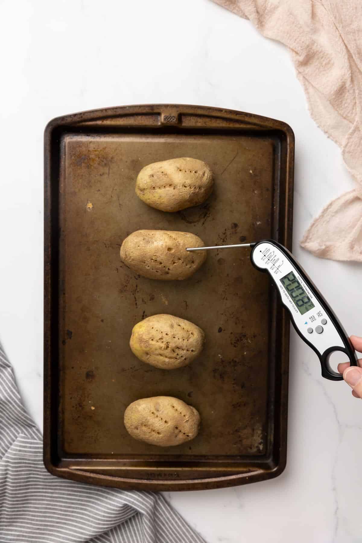 Four Russet baking potatoes on a cookie sheet.