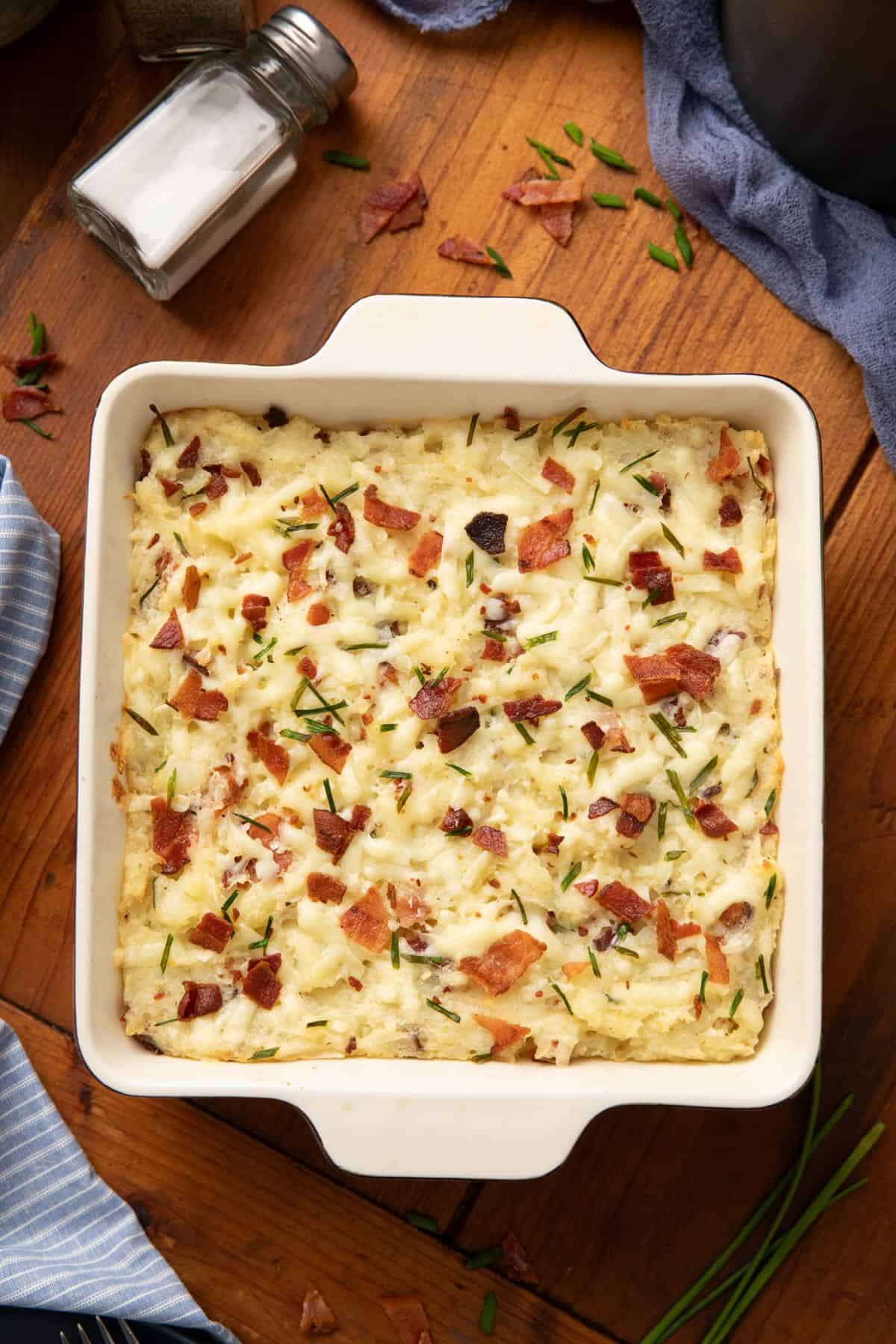 Baked Twice Baked Potato Casserole topped with melted cheese, bacon, and chopped rosemary.