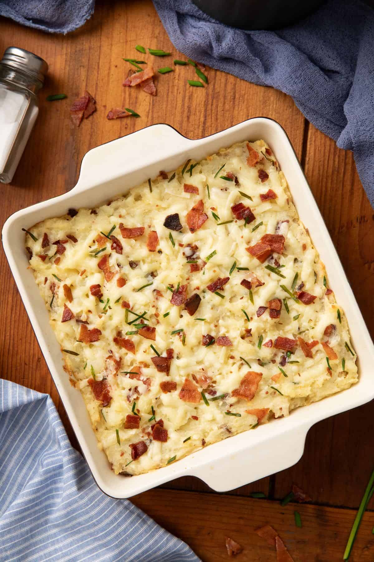 Twice Baked Potato Casserole topped with melted cheese, bacon and rosemary, ready to serve.