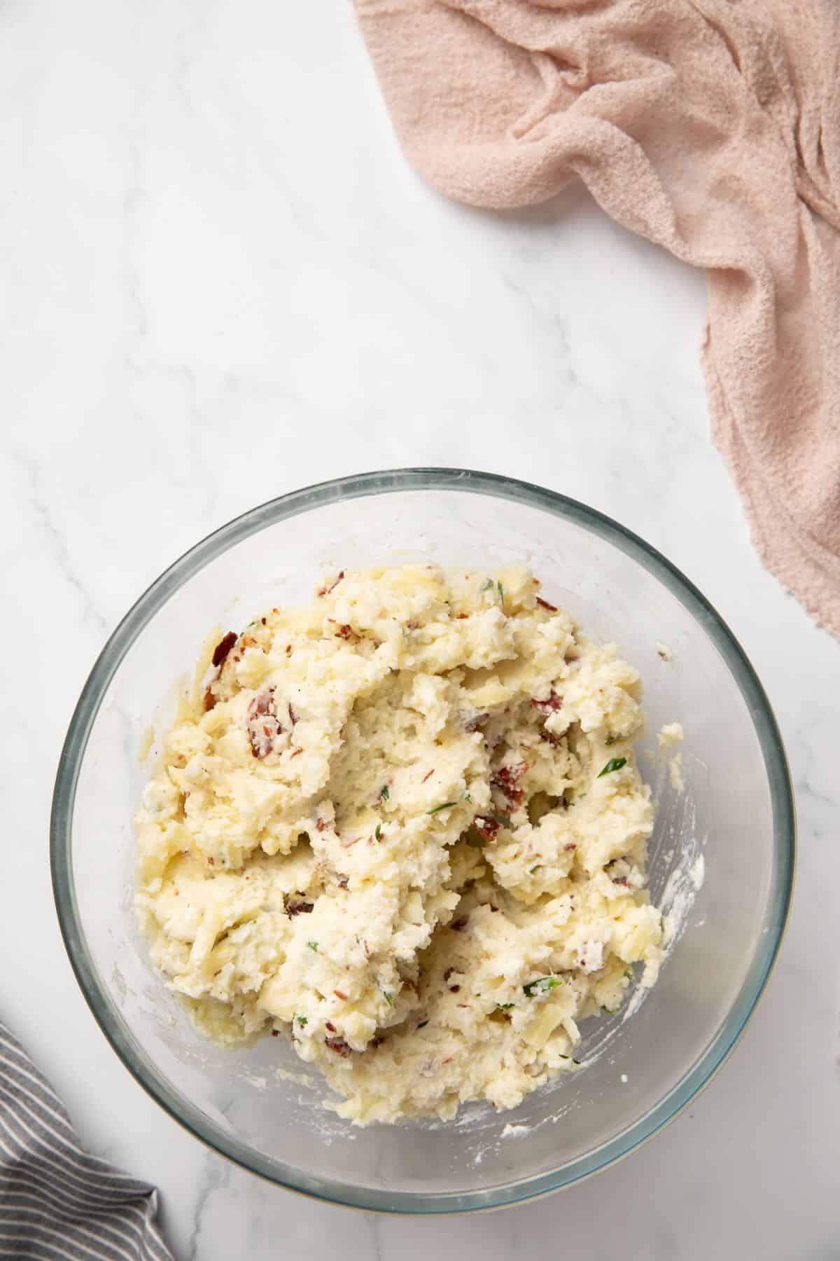 Mashed baked potatoes with cream, sour cream, bacon, and cheese in a bowl.