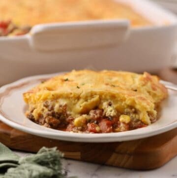 A serving of cowboy cornbread casserole on a plate in front of the casserole dish.