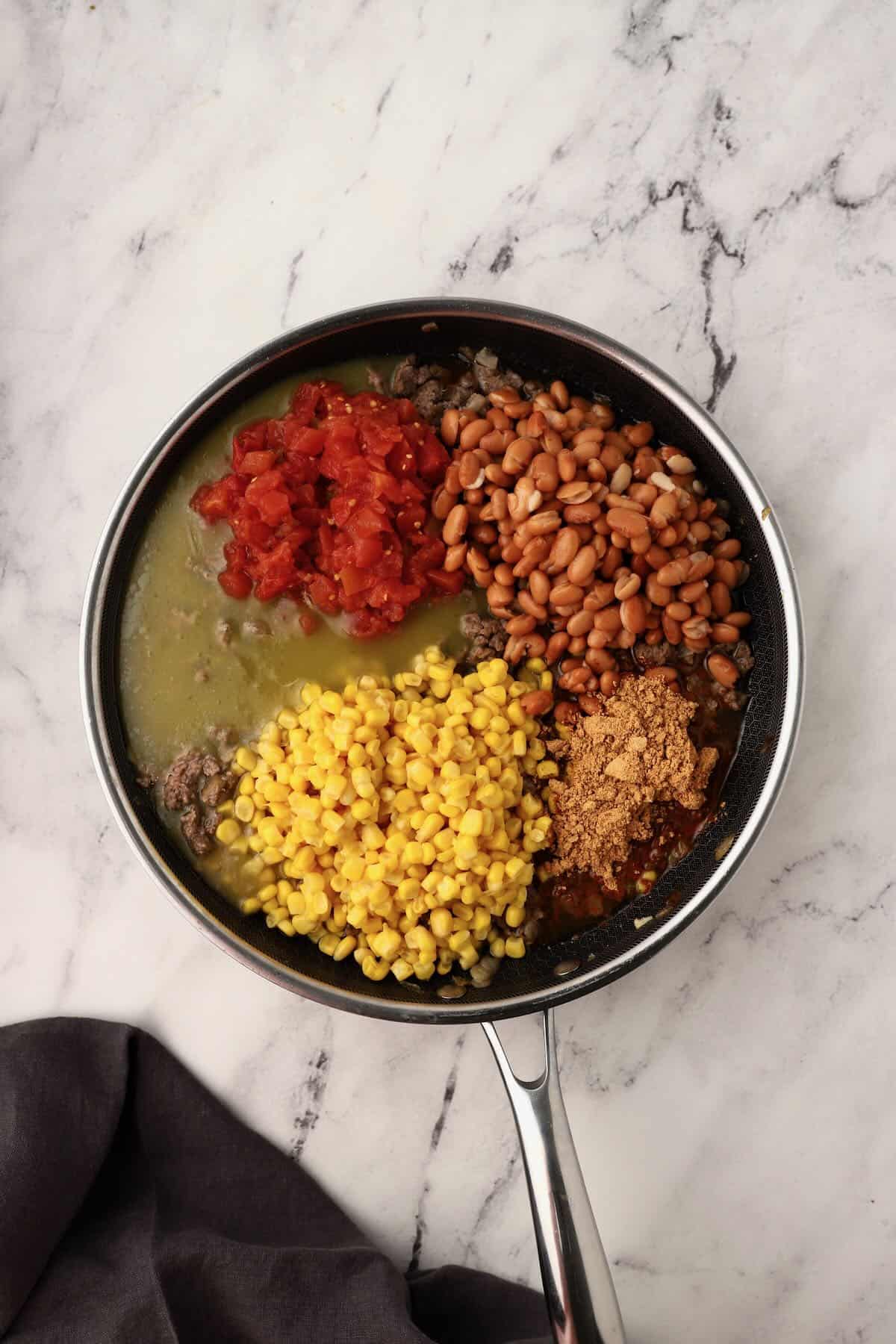 Ground beef mixture with corn, pinto beans, Rotel tomatoes, and green enchilada sauce in a skillet.