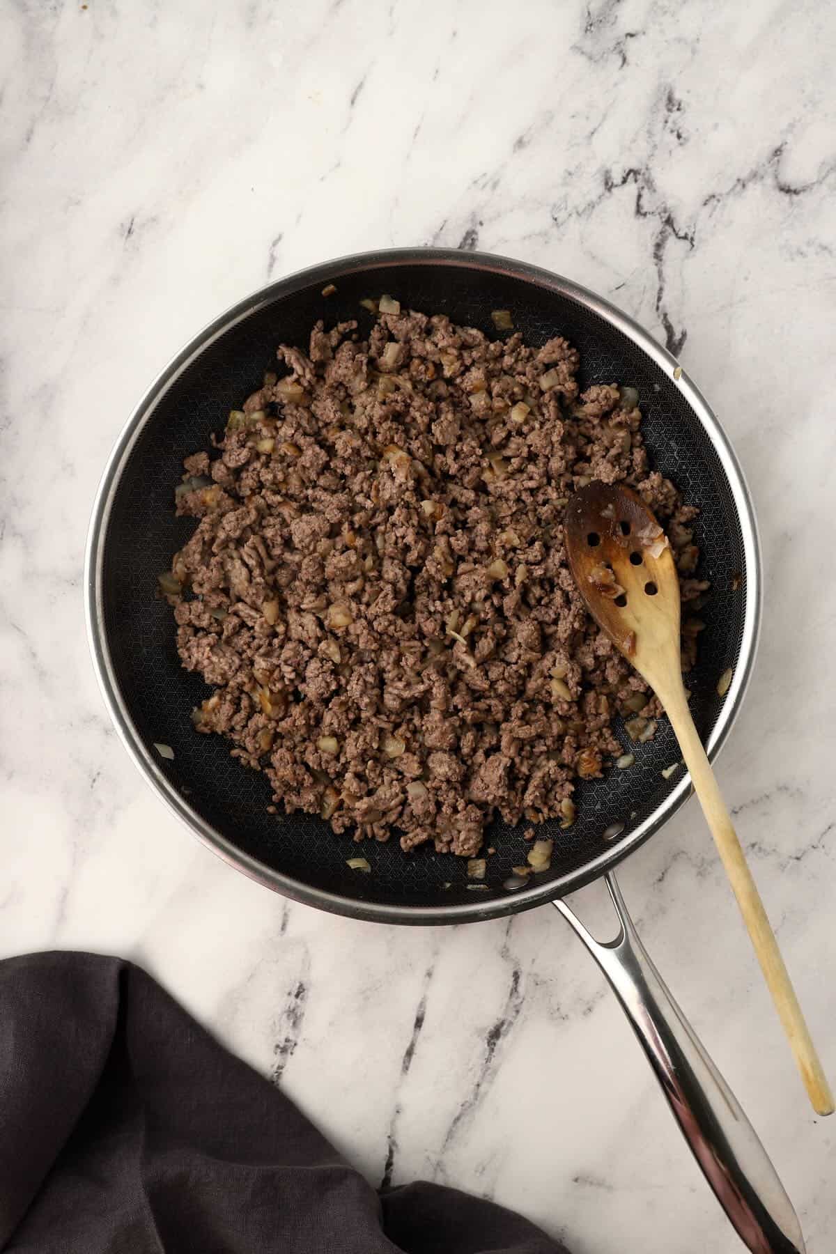 Ground beef and diced onions are browning together in a skillet.