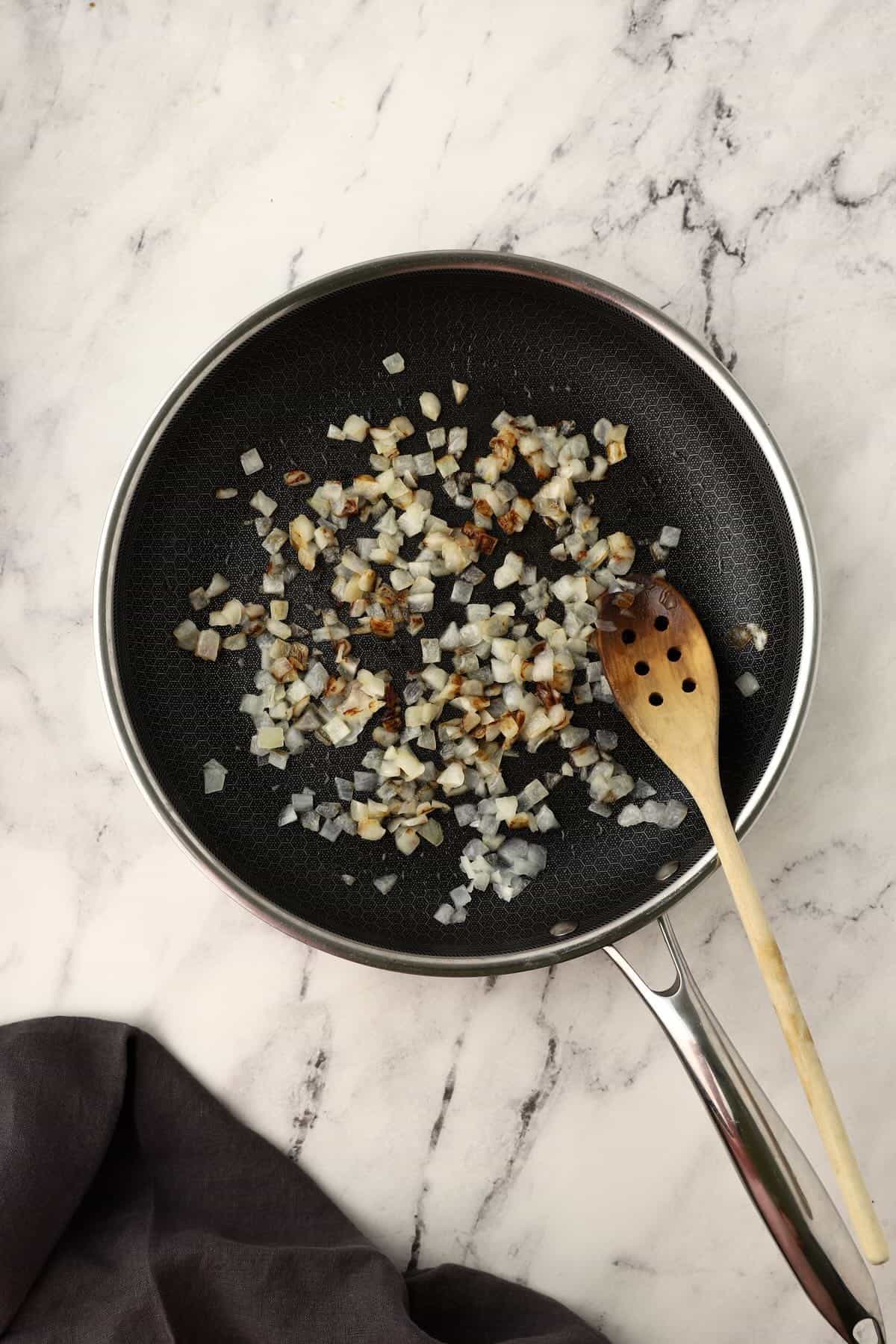 Diced onions cooking in a skillet until softened.