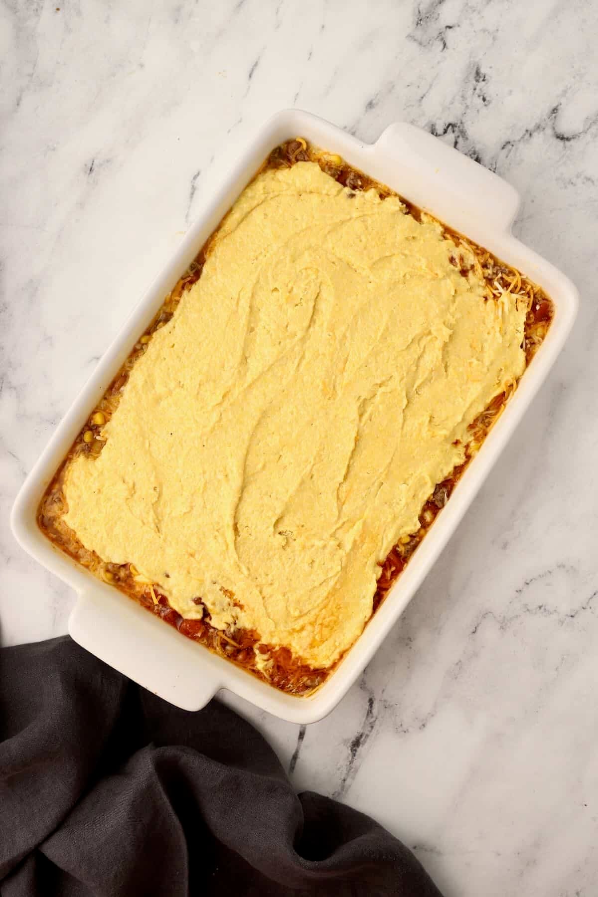 Ground beef casserole filling covered with Jiffy cornbread batter in a baking dish.