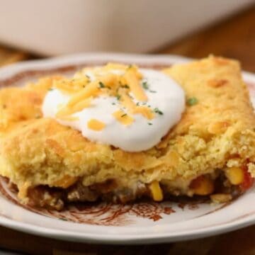 A serving of cowboy cornbread casserole topped with sour cream and shredded cheese.