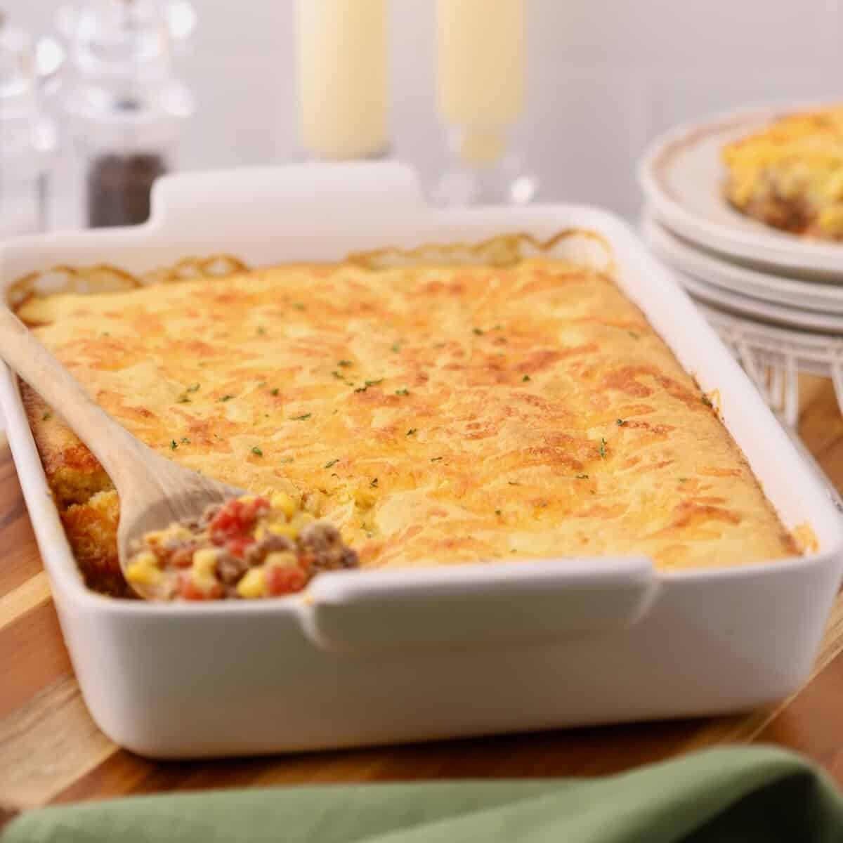 Baked Cowboy Cornbread Casserole in a white baking dish with a plated serving in the background.