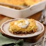 A serving of cowboy cornbread casserole on a plate in front of the casserole dish.