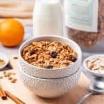 A bowl full of cranberry orange granola with milk behind it.