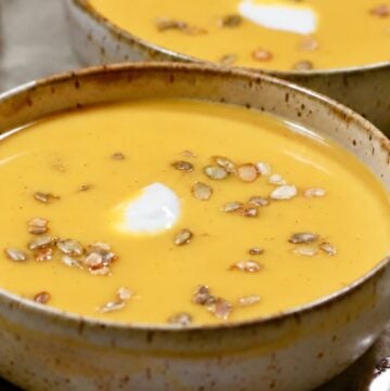 Two bowls of pumpkin sweet potato soup topped with crème fraîche and pepitas.