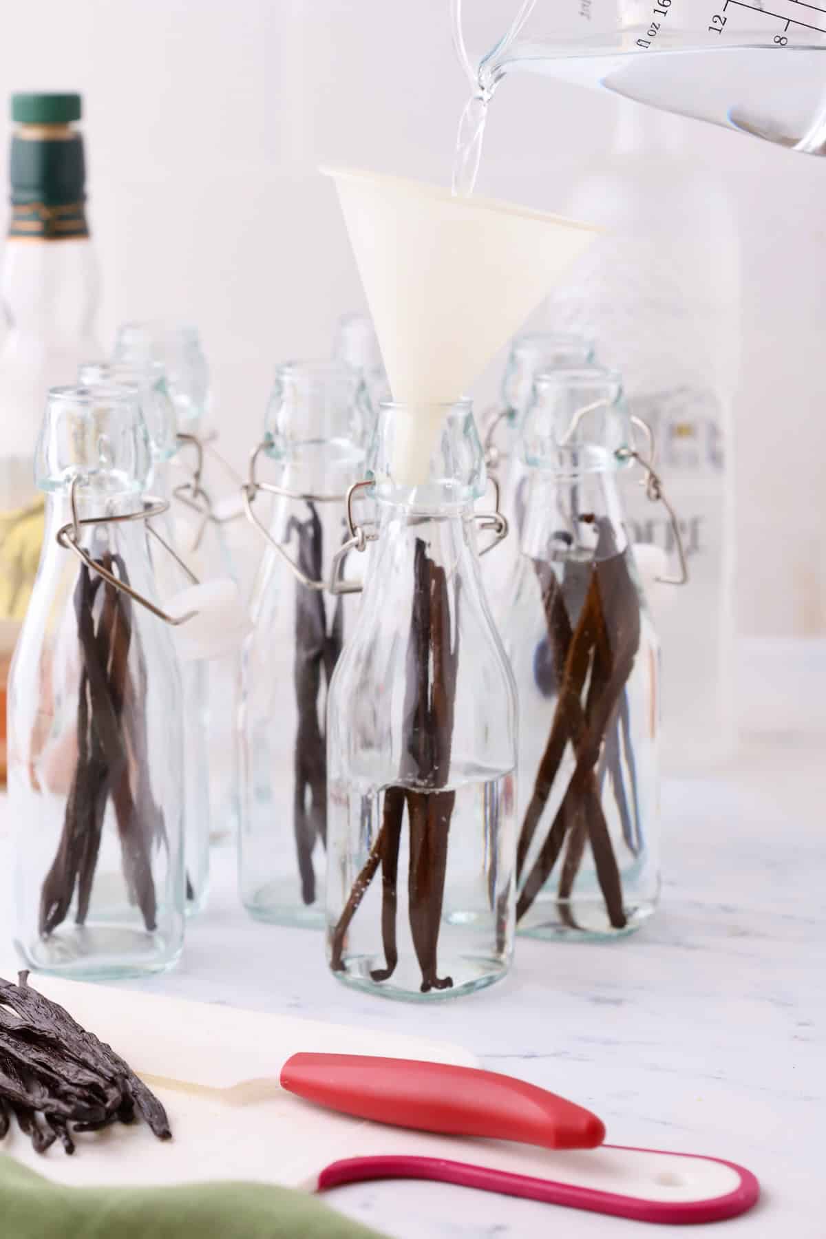 Filling glass jars with vodka using a funnel.